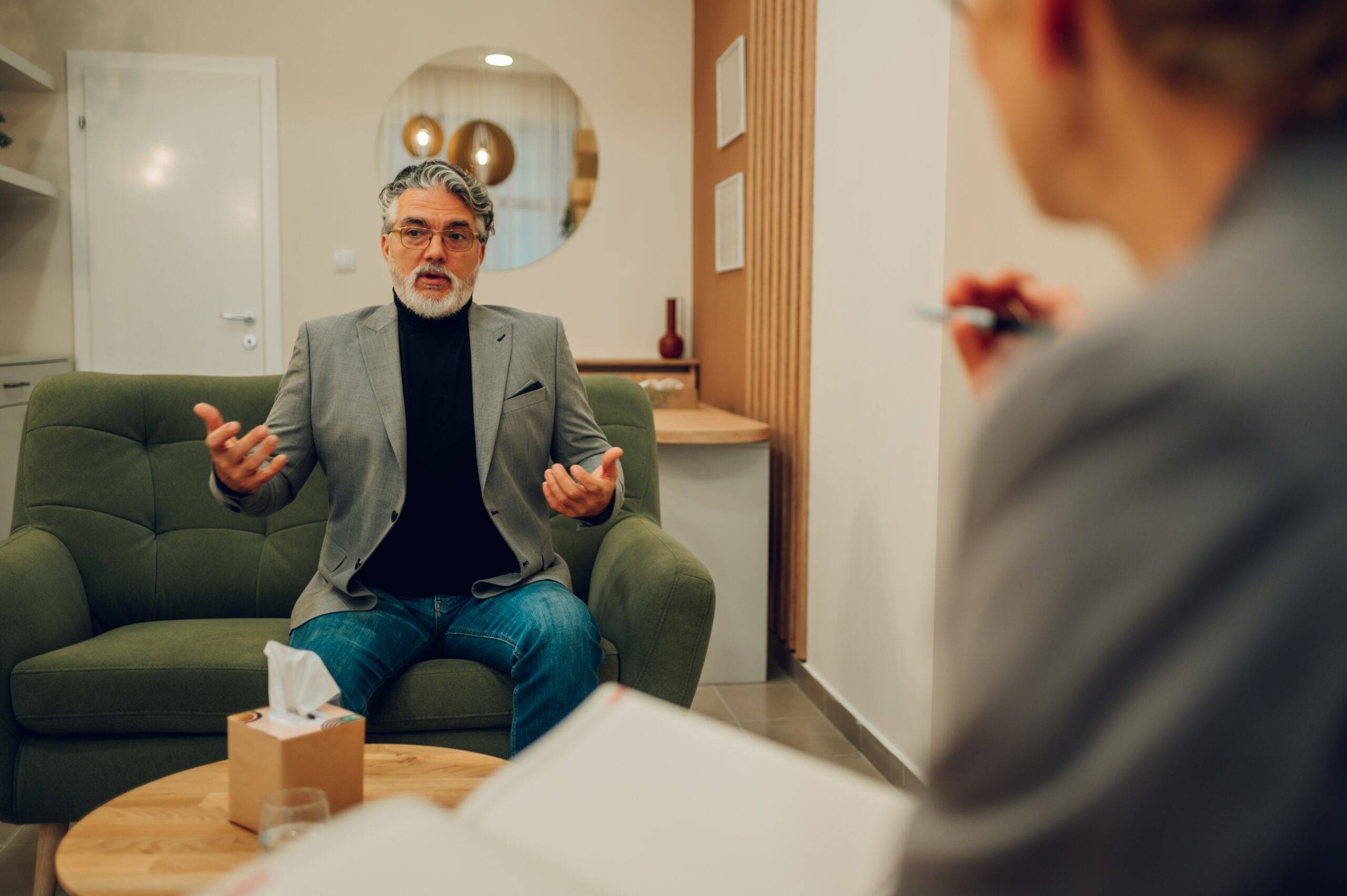 man on green couch explaining his life's challenges to a male counsellor sitting in an opposite facing chair