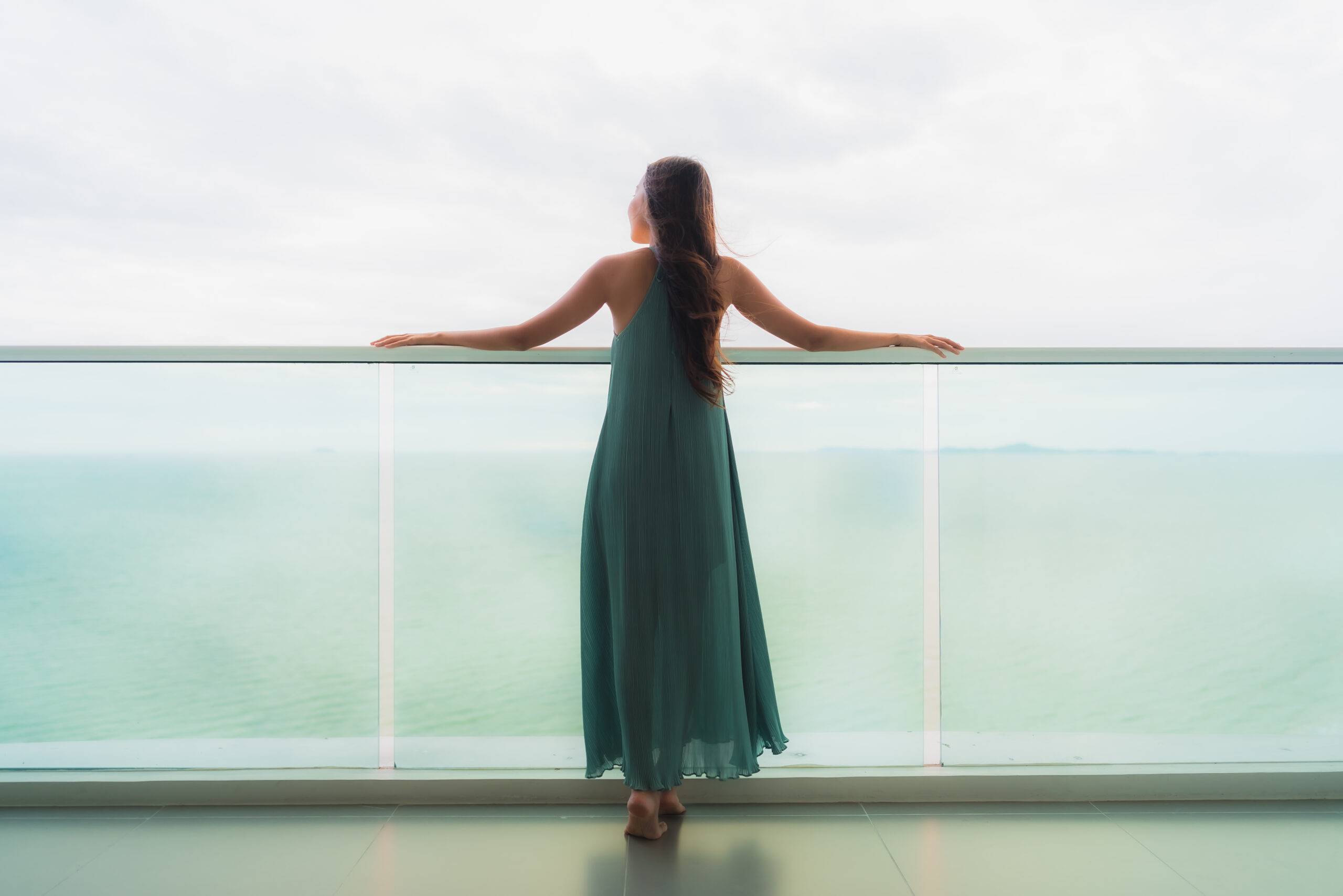 young woman in green dress looking out over a glass balcony