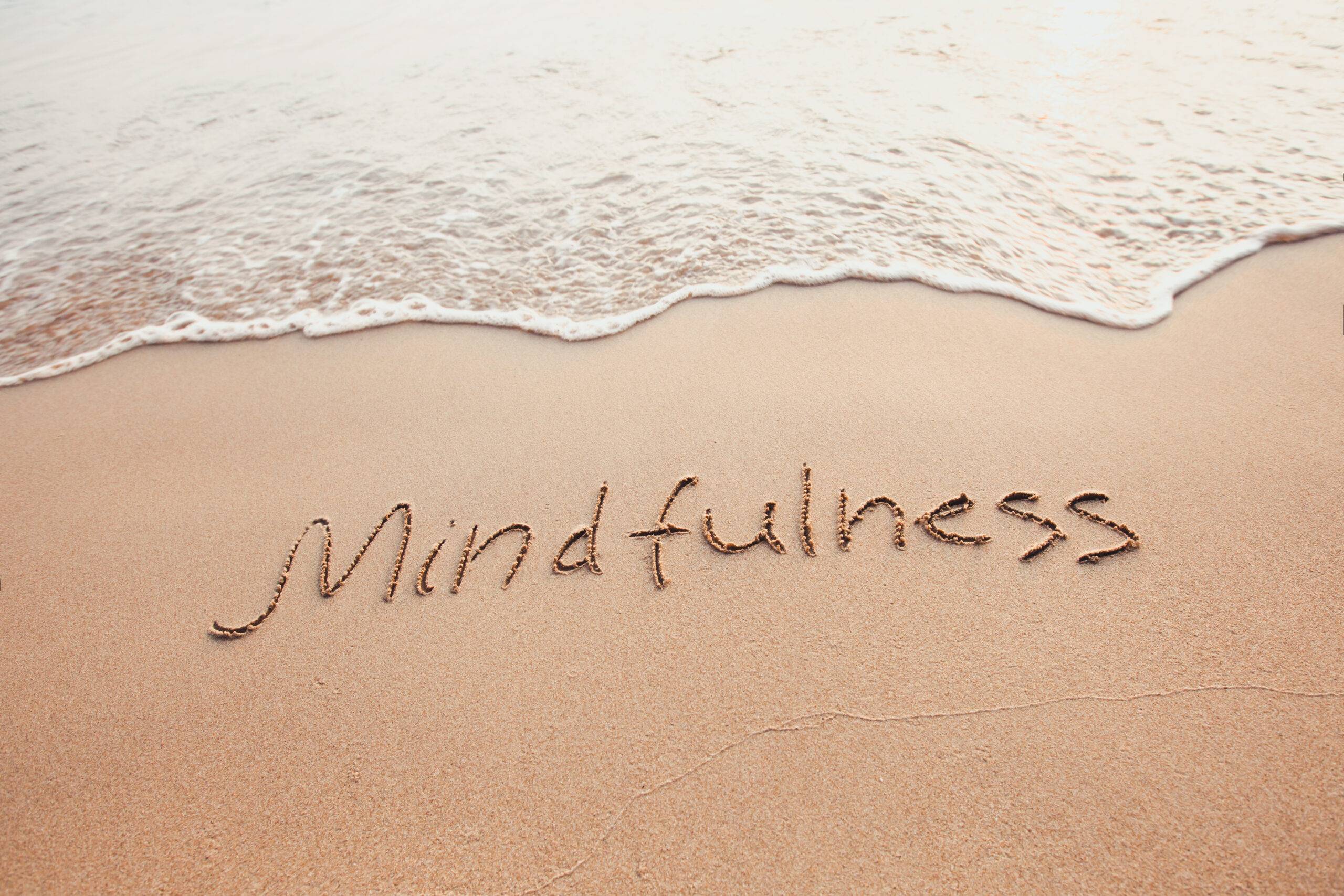 light brownish yellow sand beach with the word mindfulness written with a stick in the san