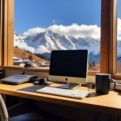 computer on a desk overlooking a snow capped mountain on a sunny day